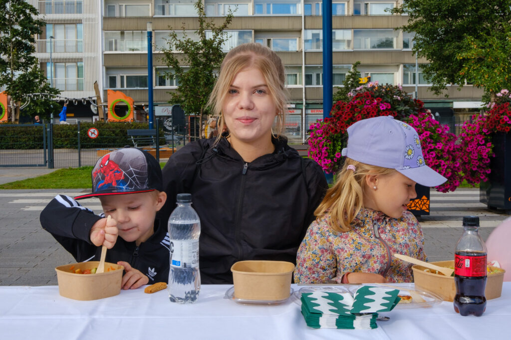 Perhe ruokailemassa puistossa pöydän ääressä.