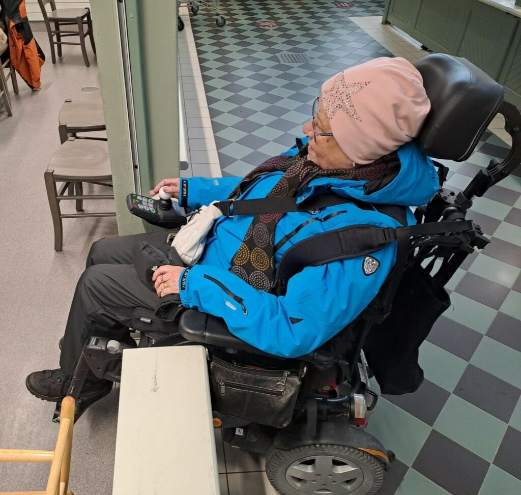 Vammainen ihminen yrittämässä mennä sähköpyörätuolilla oviaukosta.