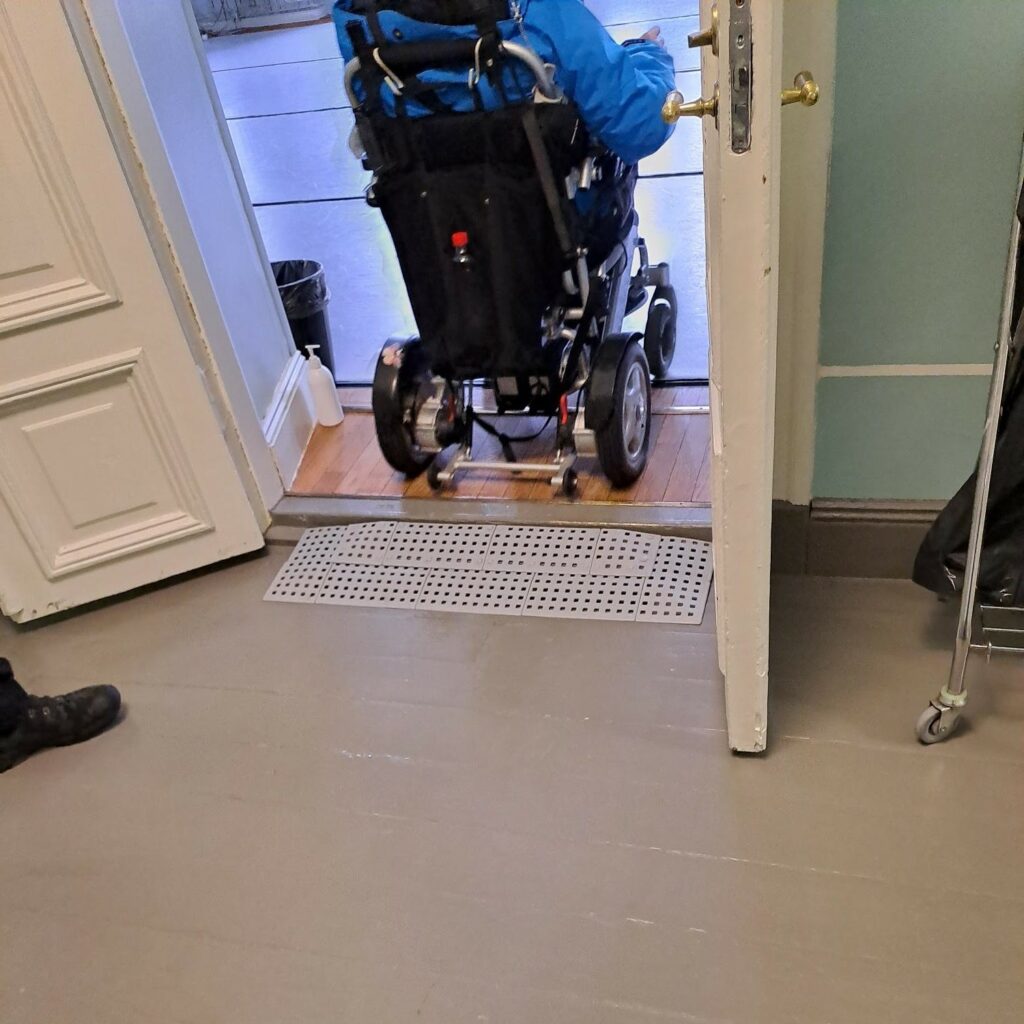 Henkilö ylittää kynnyksen sähköpyörätuolilla kulttuuritalo Valveen oviaukolla luiska apuvälineenään.