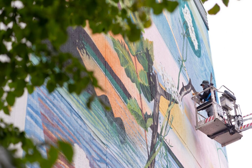 Fabio Petani on a crane painting a mural on a building wall