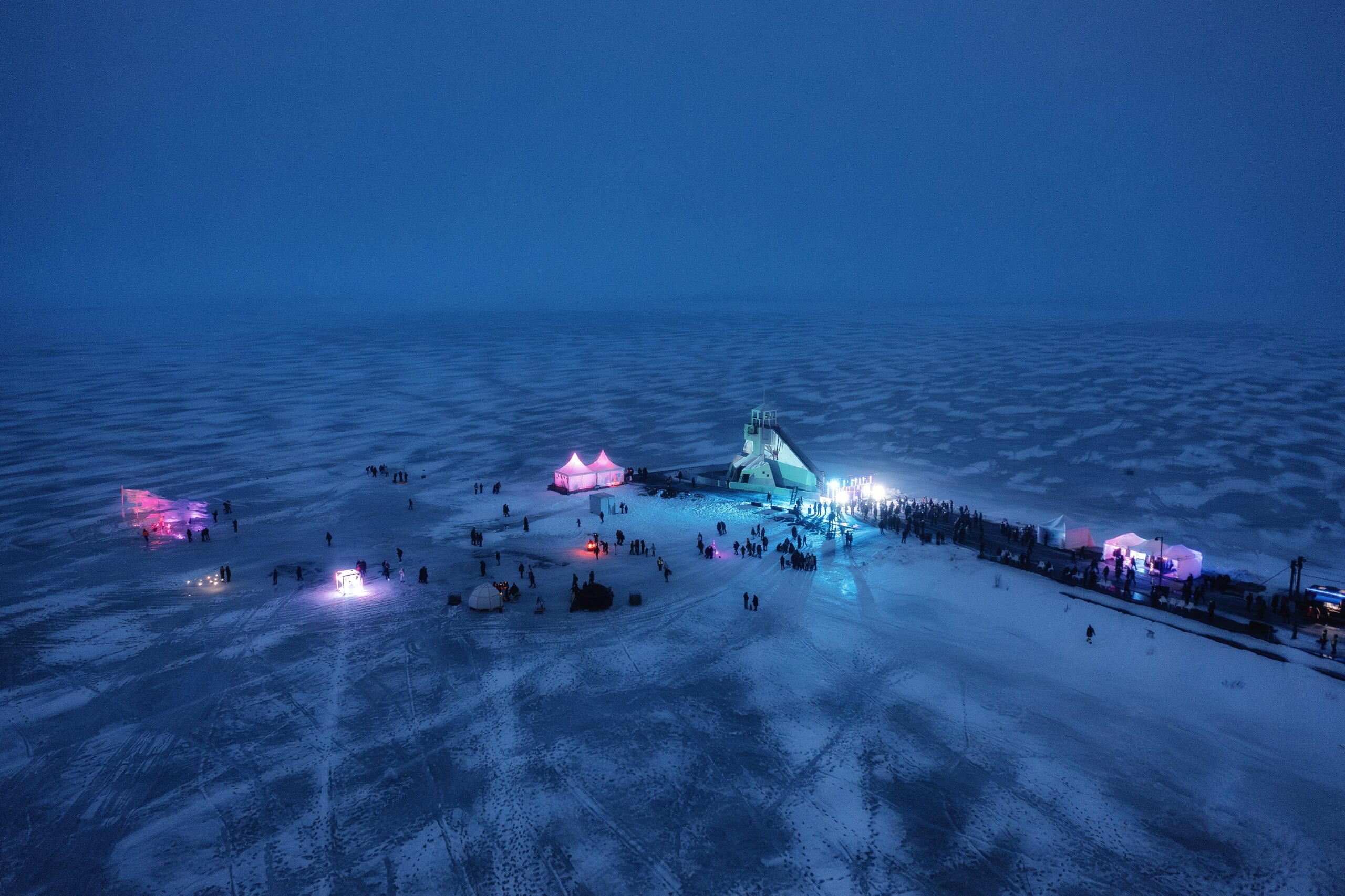 Illuminated tents on frozen lake at night.