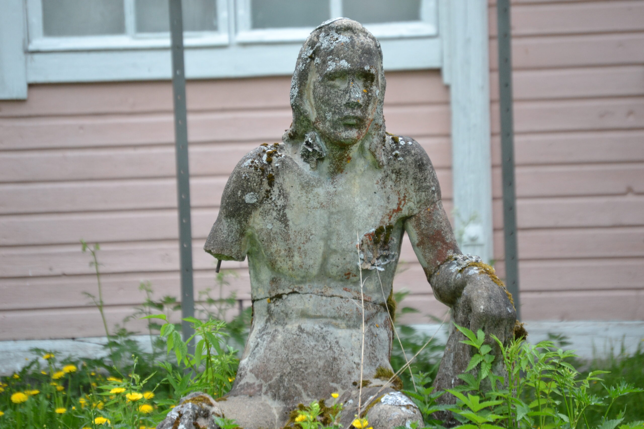 Kuvassa kesäisessä ulkotilassa ränsistynyt, istuvaa ihmistä kuvaava patsas. /valokuvaaja Minerva Asamäki/ 2024/Kuvistuskuva