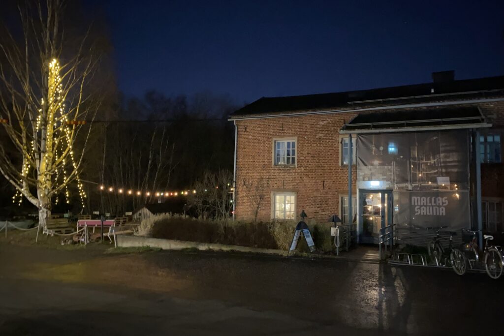 Tiilirakennus iltavalaistuksessa, valoja pihalla. Mallassauna