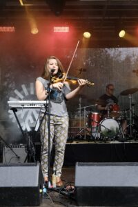 Viulisti esiintyy ulkoilmakonsertissa lavalla rumpalin kanssa.