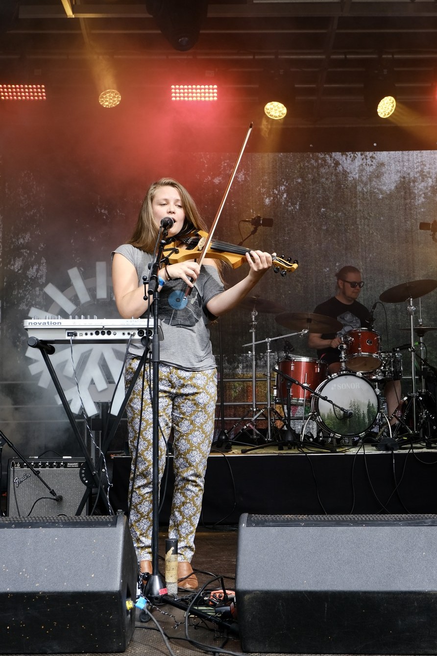 Viulisti esiintyy ulkoilmakonsertissa lavalla rumpalin kanssa.