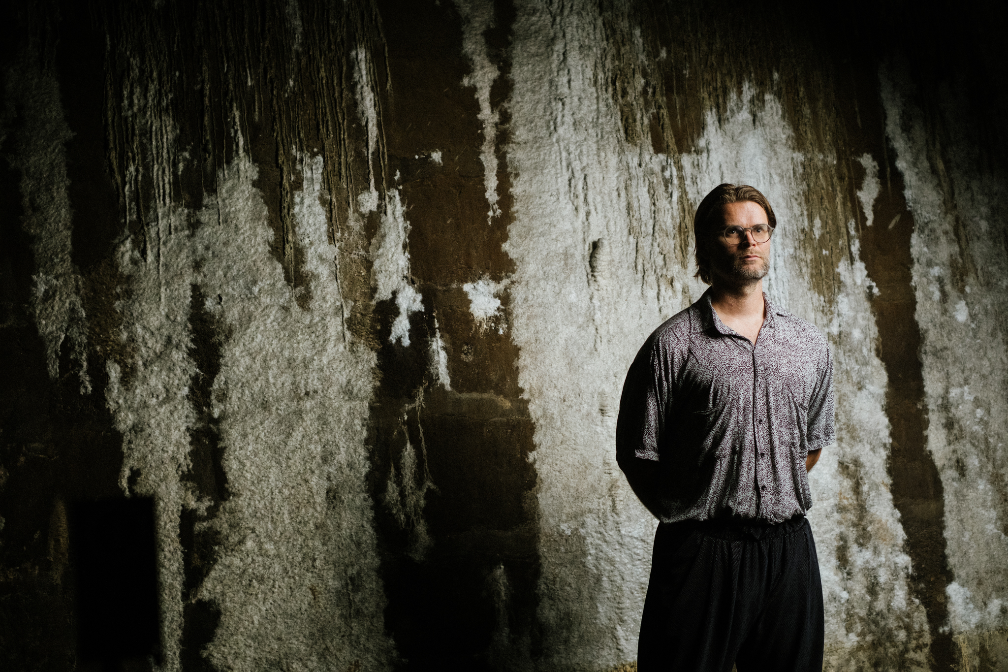 Jakob Kudsk Steensen standing against textured wall, dimly lit scene.
