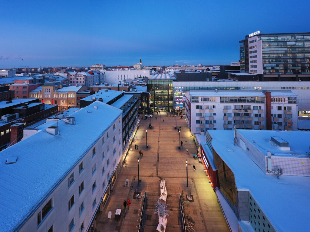 Snowy cityscape with illuminated buildings and pathway.