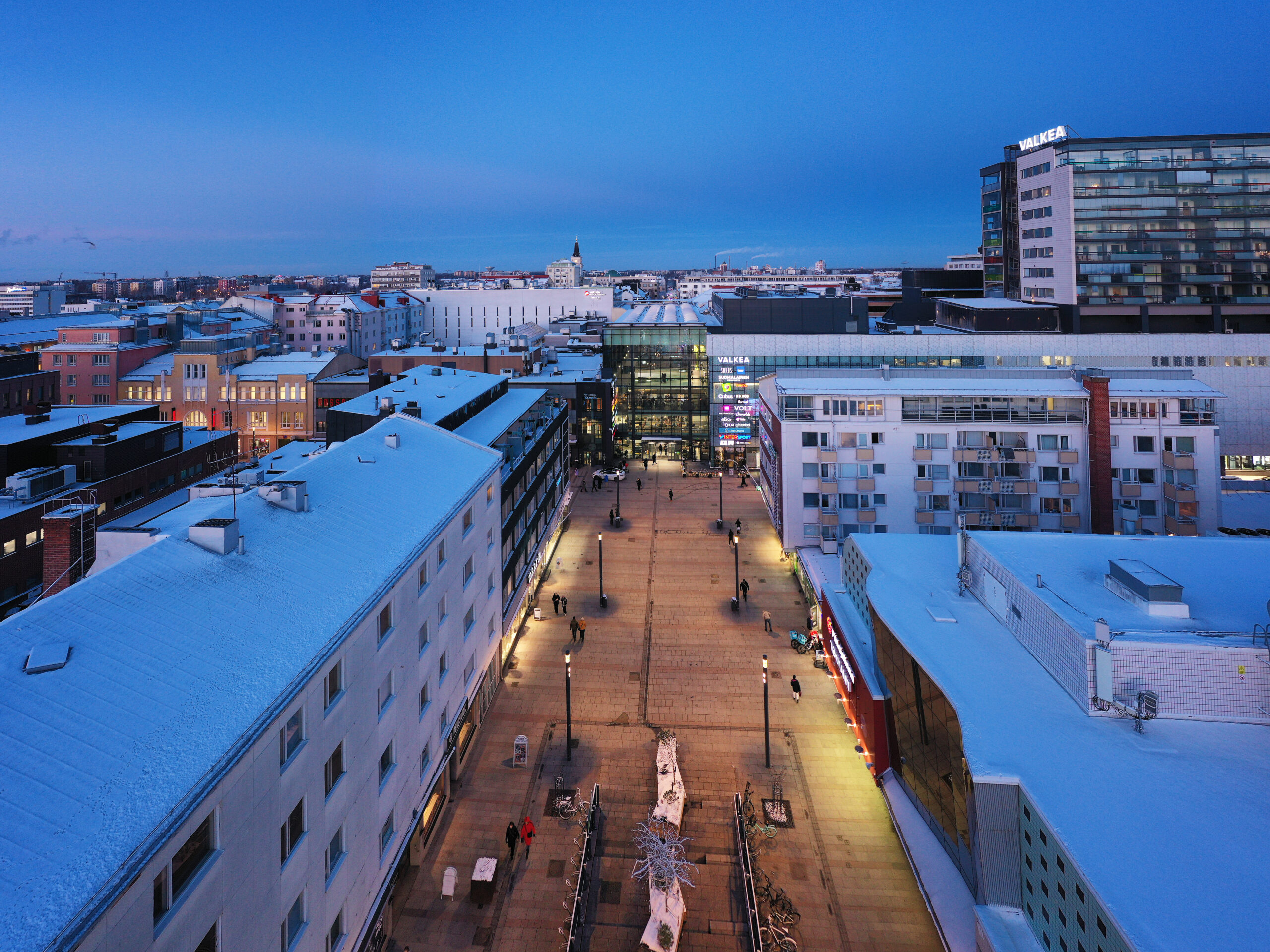 Snowy cityscape with illuminated buildings and pathway.