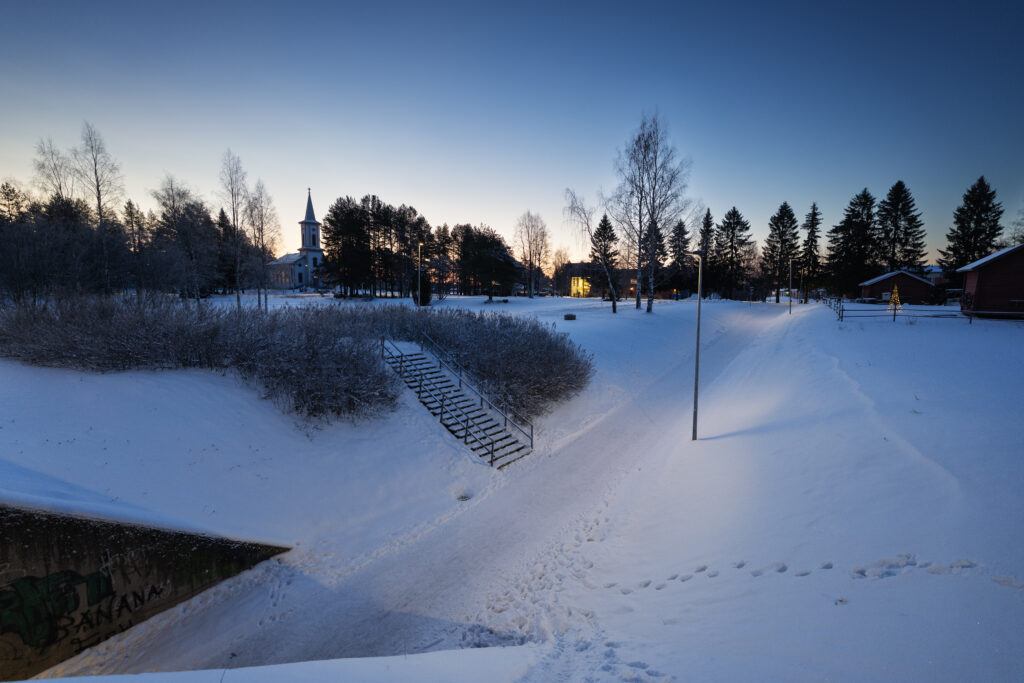 Snowy village landscape at dusk with church.