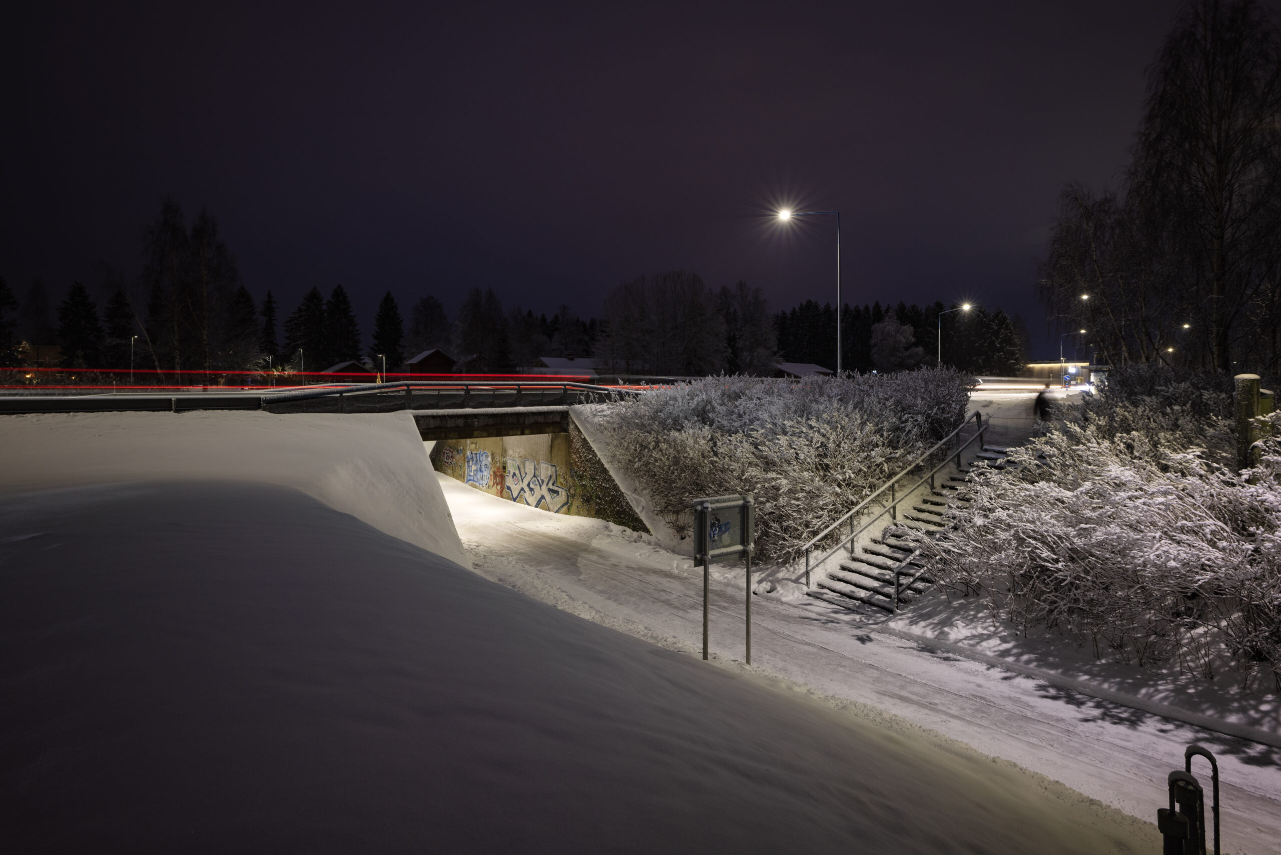 Snow-covered pathway under bridge at night.