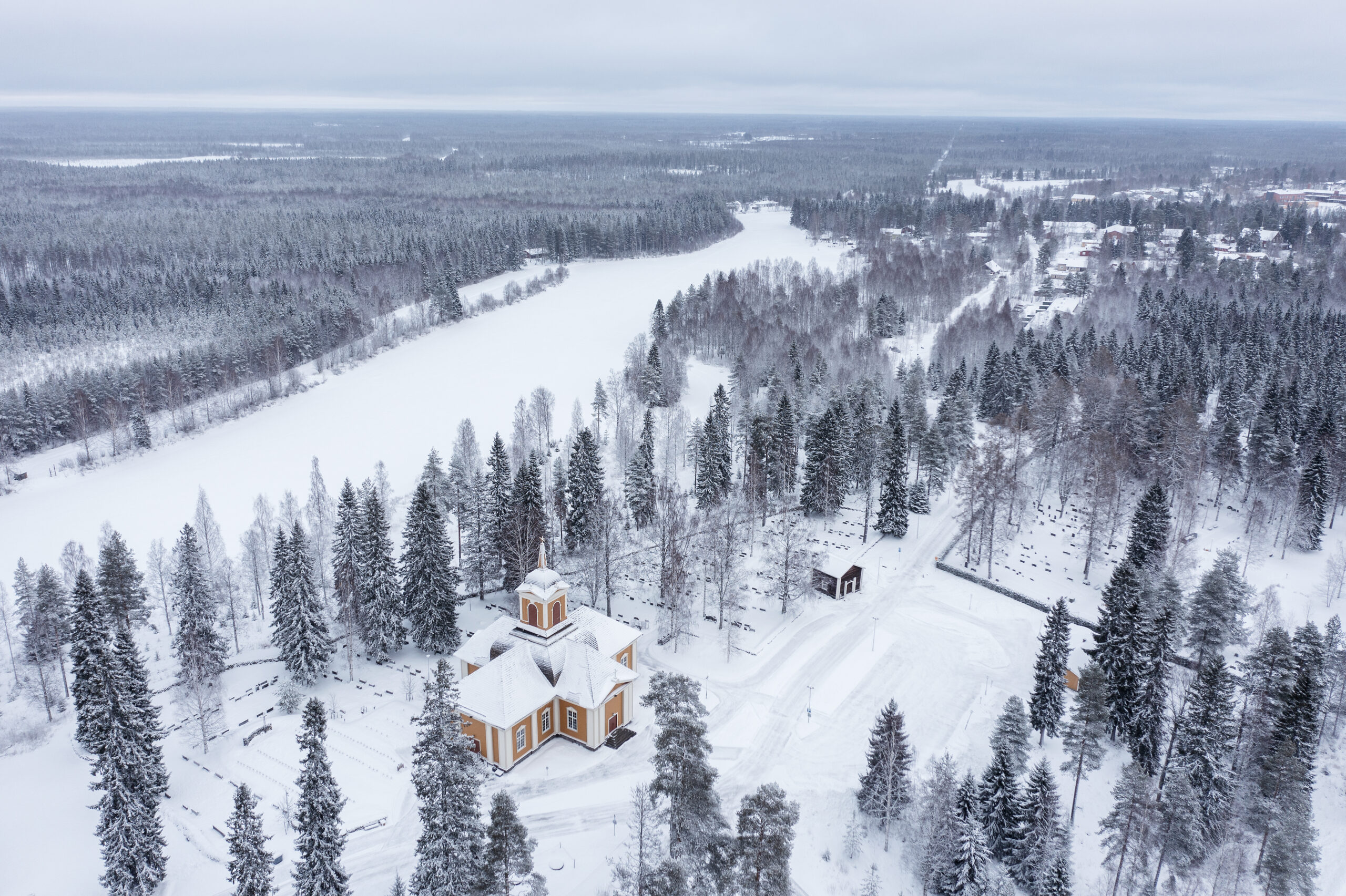 Snowy landscape with forest and small church.