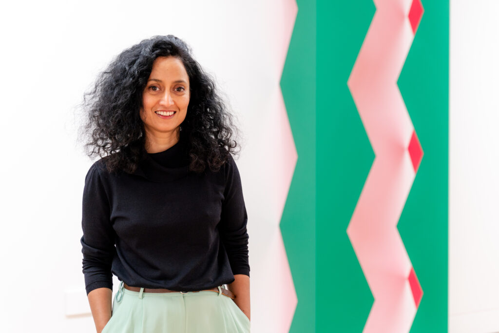 Smiling woman beside colourful geometric artwork.