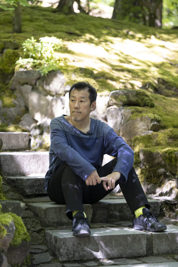 Man sitting on stone steps in wooded area.