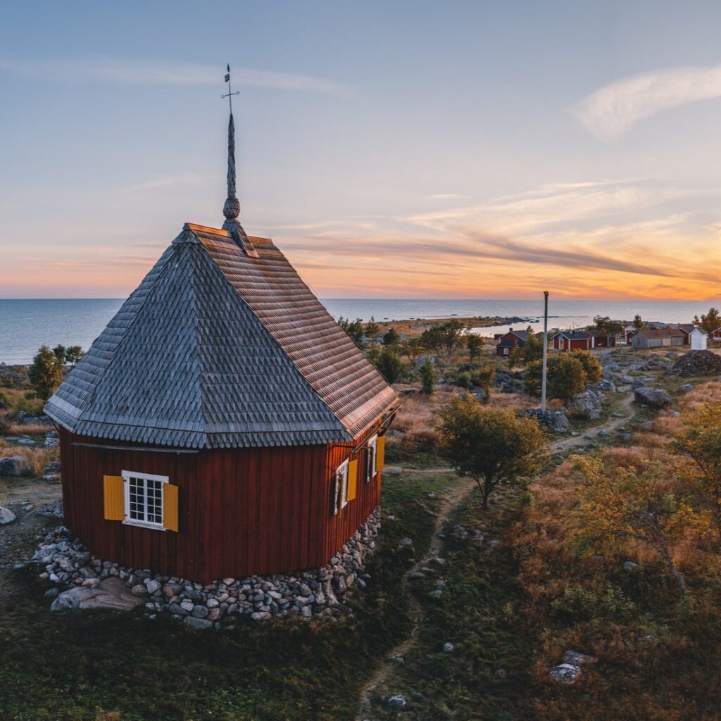 Punainen mökki merenrannalla auringonlaskun aikaan.