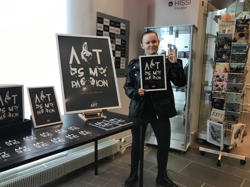 Taiteilija Maarit Ylitalo käsissään Art is my passion -juliste taidemuseon kaupassa.